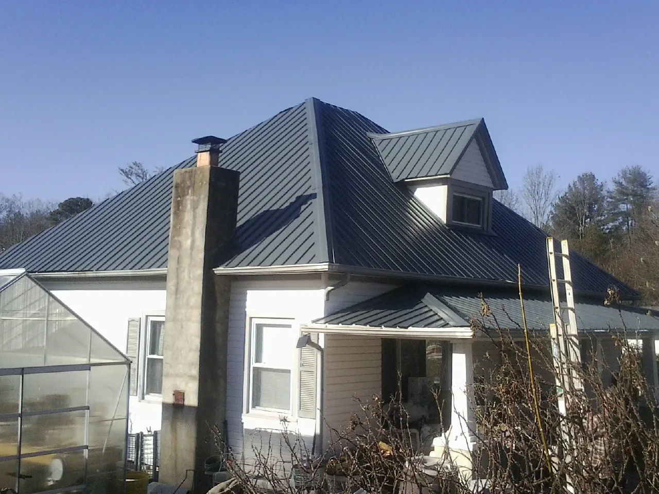 Dark blue standing seam metal roof on a white farmhouse with dormer — Slate & Tile Roof Repair by Roofing Brothers in Laurier
