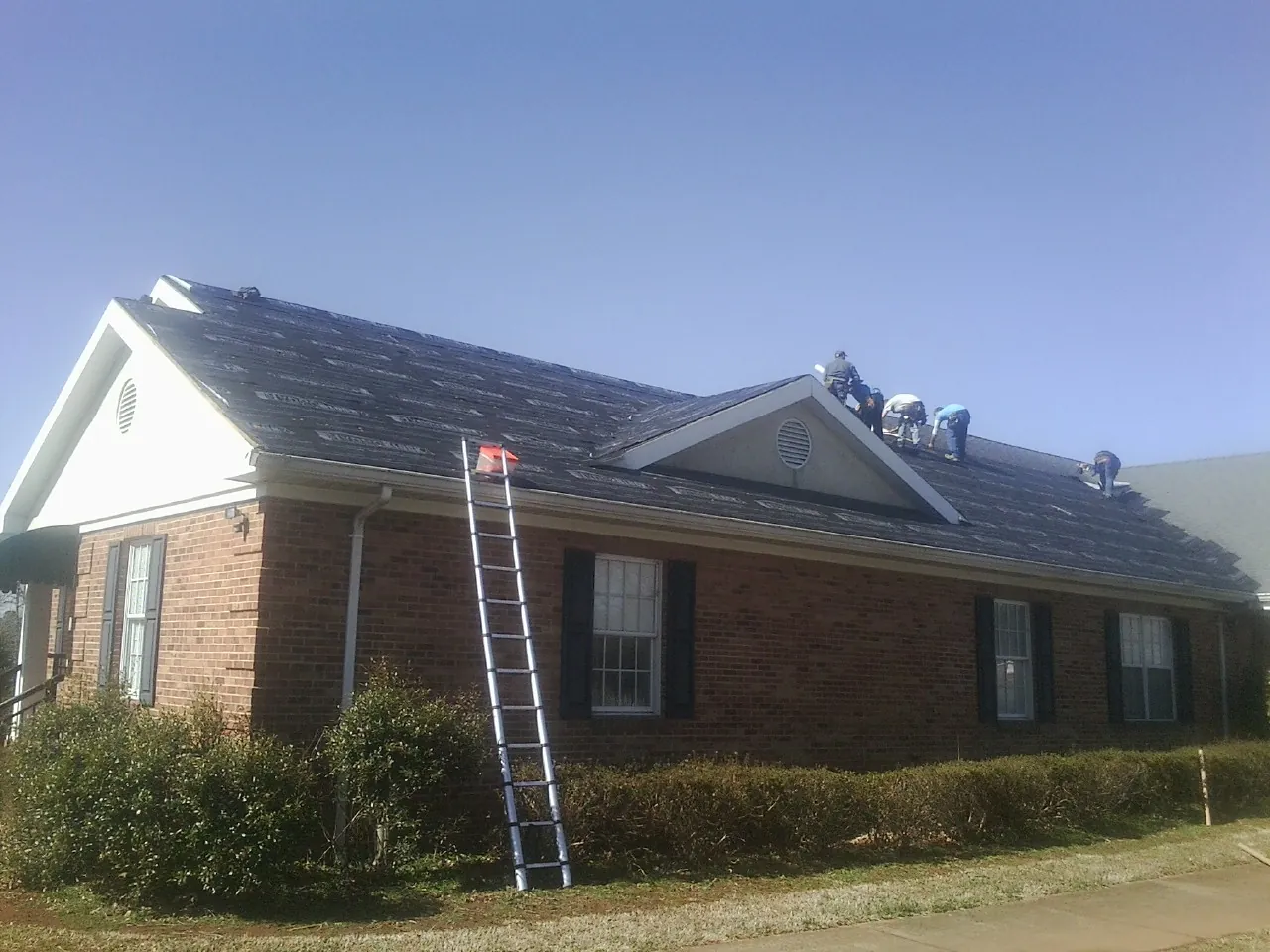 Crew tearing shingles off a brick ranch roof with a ladder set — Emergency Roof Repair work by our crew in Laurier