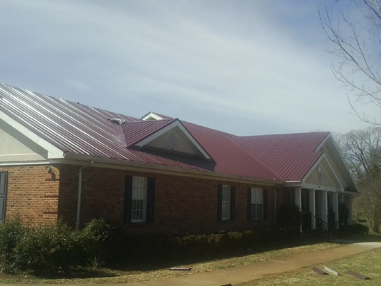 Red metal roof with gabled entries on a long brick building, from a Hail Damage Roof Repair job in Laurier