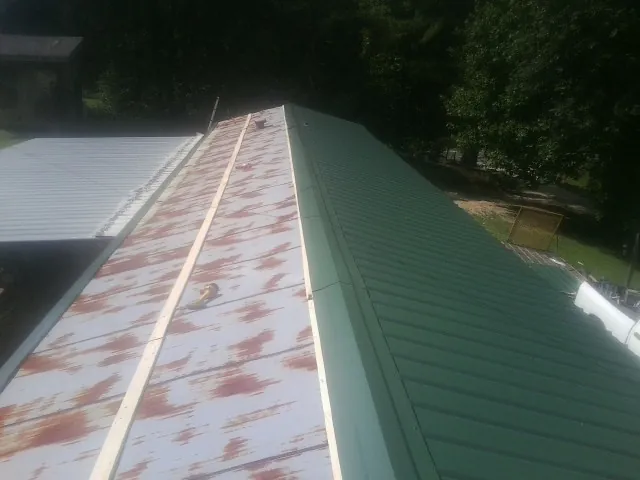 Old rusted panels beside newly installed green metal roofing — Wind Damage Roof Repair by Roofing Brothers in Laurier