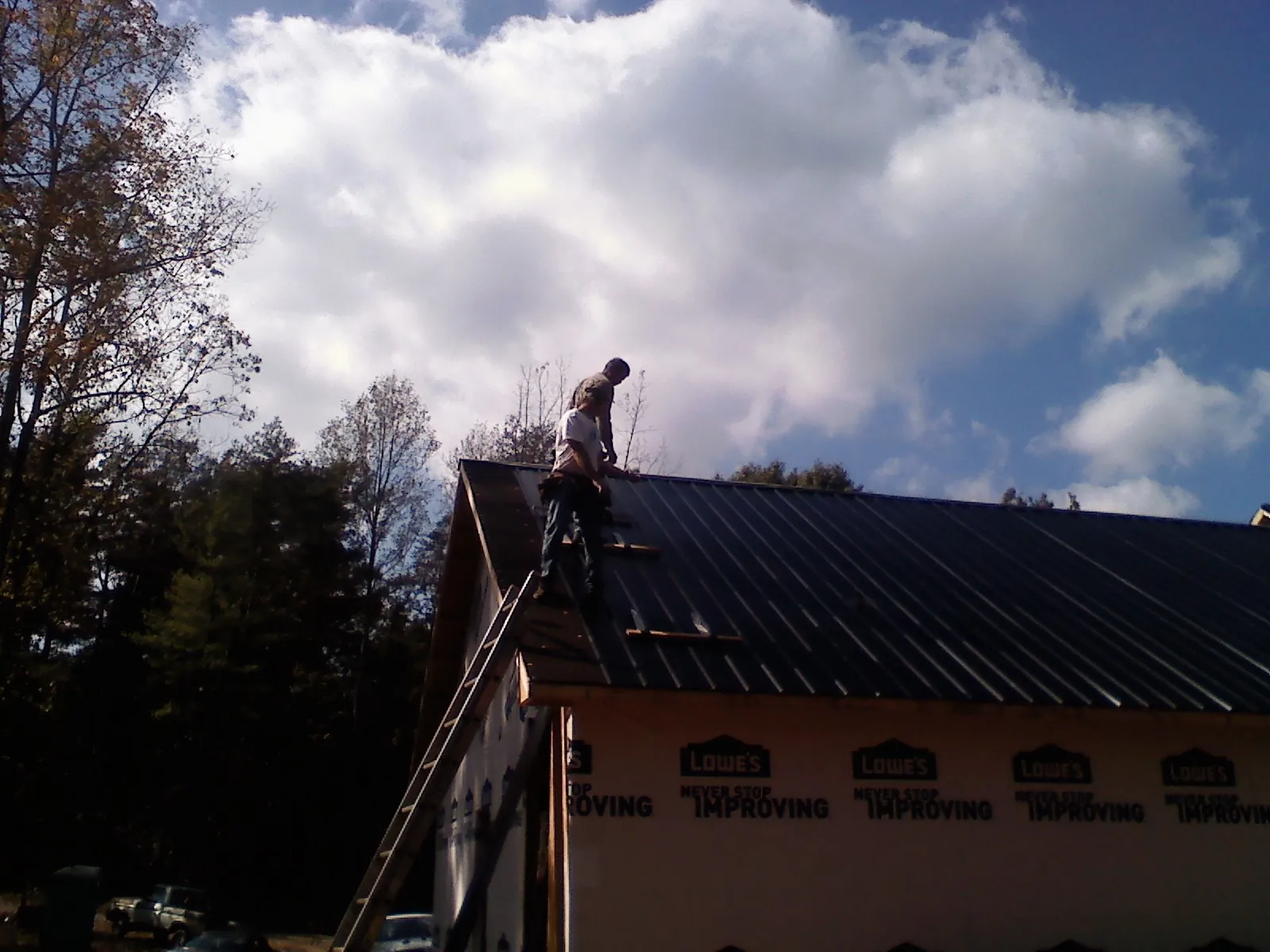 Roofer fastening dark metal panels high against a cloudy sky, from a Roof Inspection job in Laurier