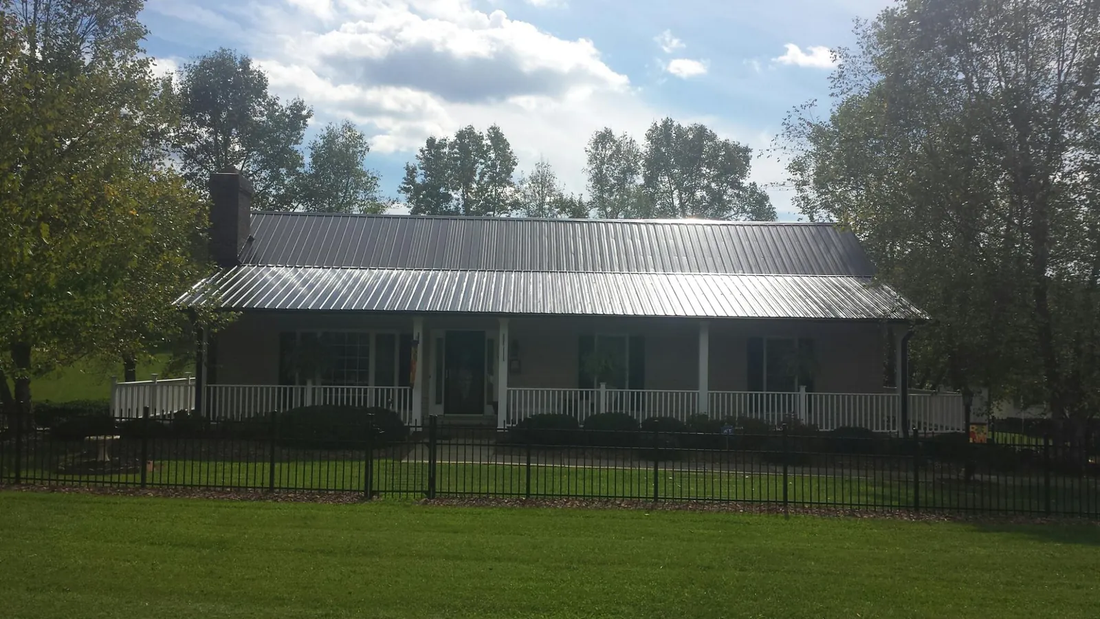 Gray metal roof on a brick ranch with a full width front porch — Gutter Guard Installation work by our crew in Laurier