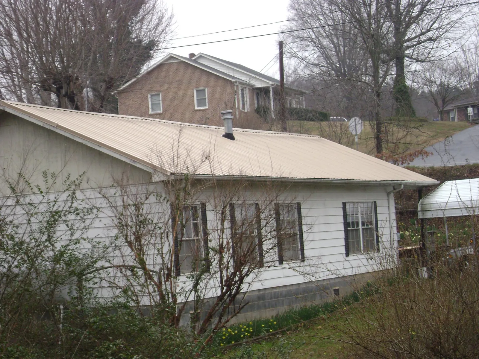 Tan metal roof on a white sided house set into a hillside — Commercial Roofing by Roofing Brothers in Laurier