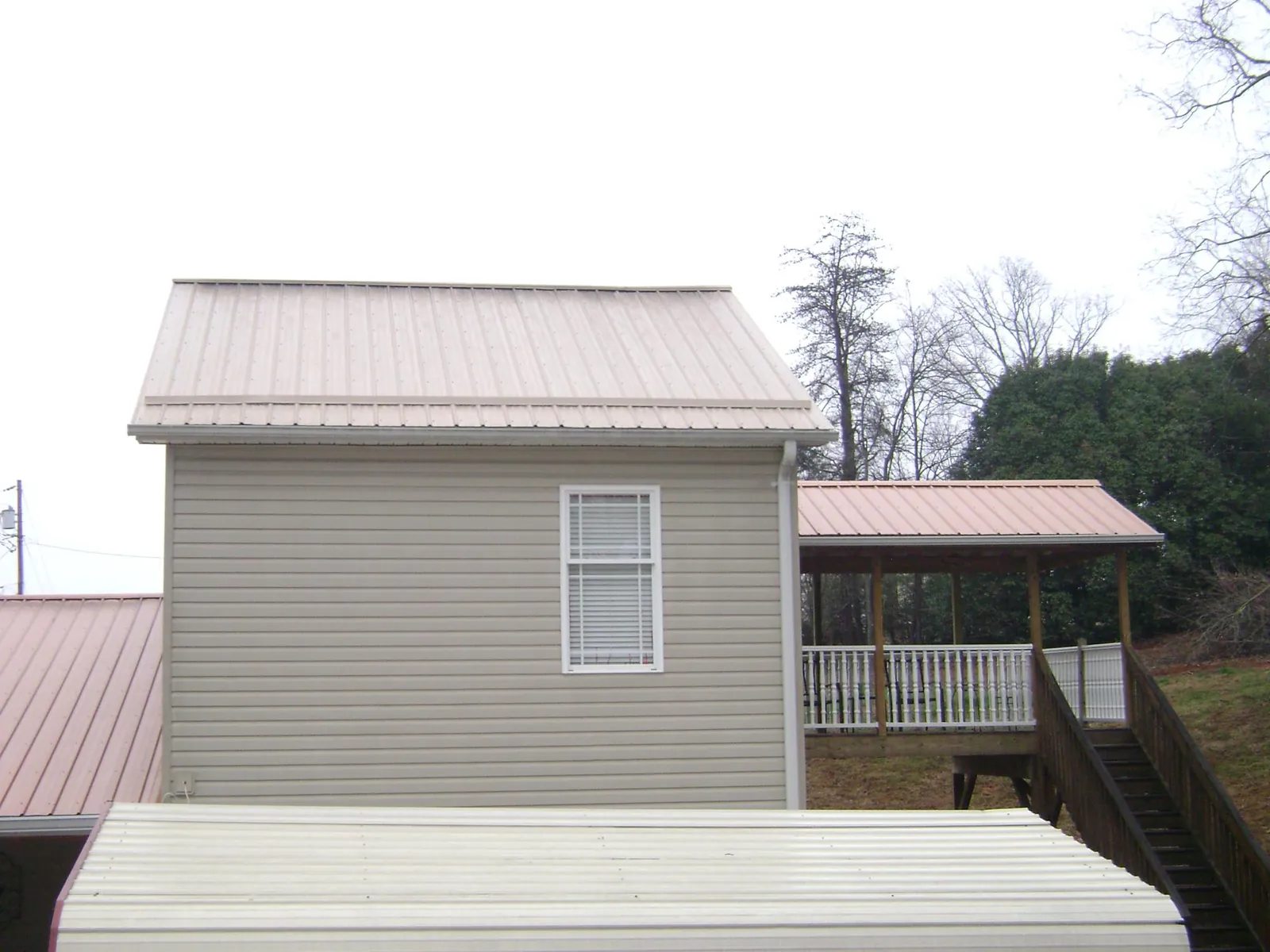 Tan metal roofs on a two story addition and attached porch, from a Roof Replacement job in Laurier